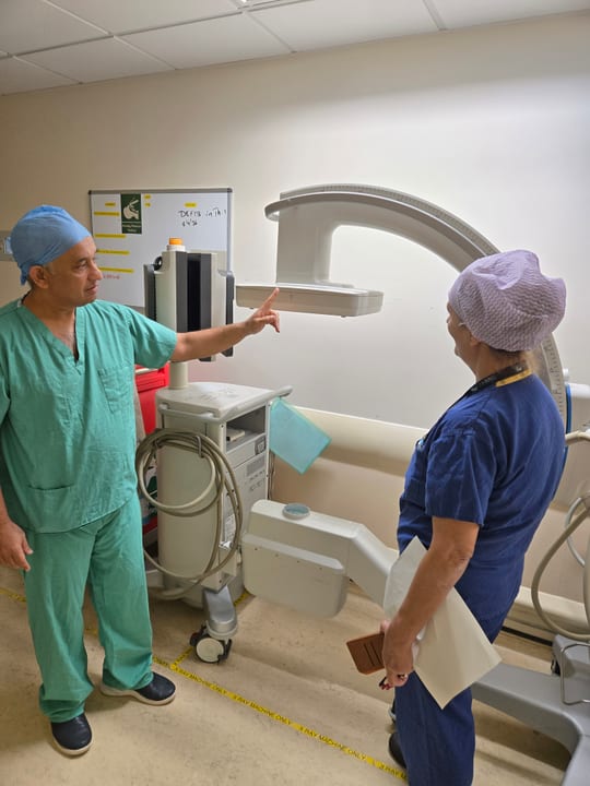 Dr. Harshawardhan Godbole in theatre scrubs pointing to a C-arm X-ray unit